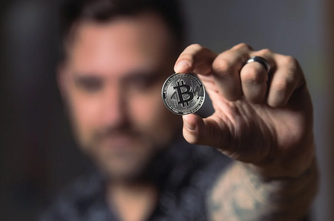 blurred photo of a man holding a Bitcoin coin